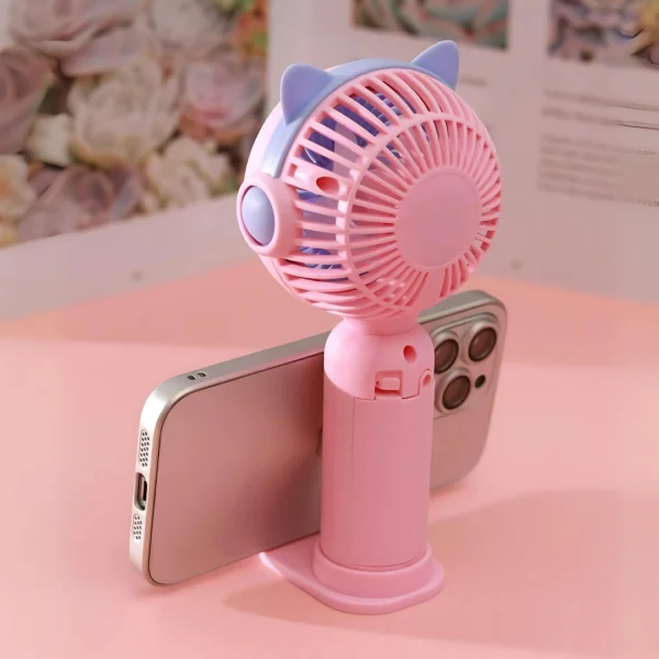 un pequeño ventilador que sirve además como soporte para celular en color rosado